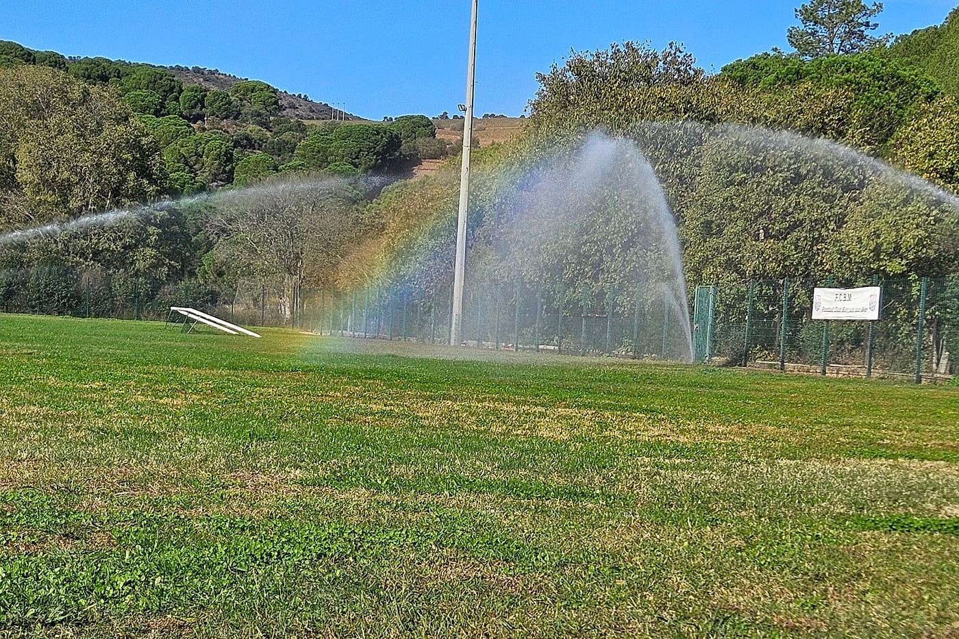 Arroseur automatique en action sur le terrain de football de Banyuls-sur-Mer, un arc-en-ciel se forme dans le jet